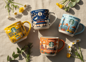 A beautiful summer flat lay display of specific Starbucks collector mugs: the Dojo mug (Japanese dojo themed), the Dijon You Are Here mug (France), the New York You Are Here discovery mug, and the Been There Guadalajara mug (Mexico). Arranged elegantly on a light warm background with subtle summer flowers and greenery. Soft natural light, vibrant colors, colorful ceramic mugs with city illustrations.
